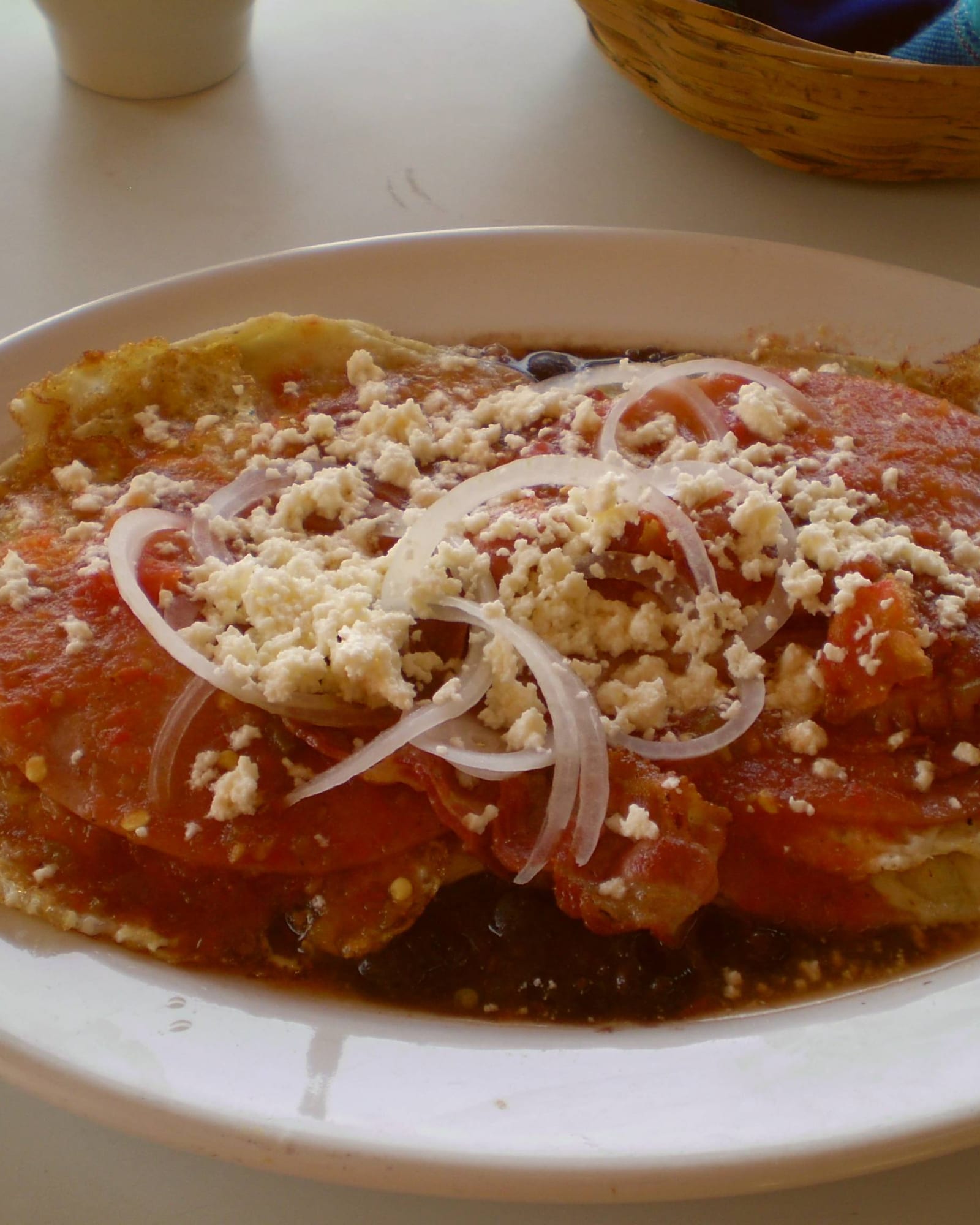 A plate of huevos rancheros topped with crumbled cheese and red salsa.