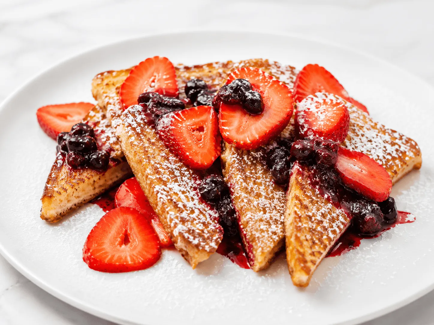 Mixed Berry French Toast topped with strawberries, berry sauce and powdered sugar